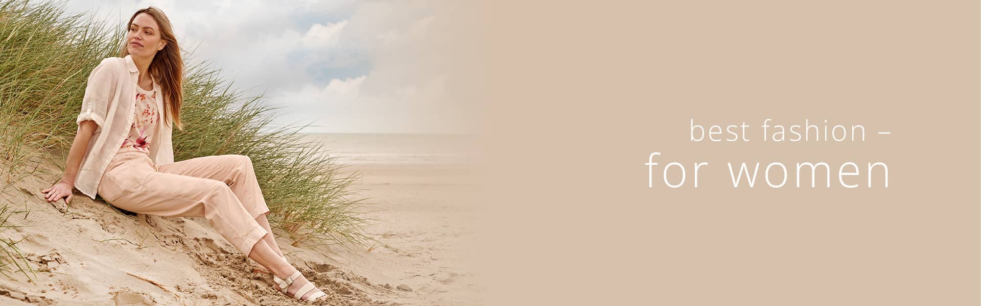 Frau am Strand mit coralfarbender Bluse und Stoffhose.