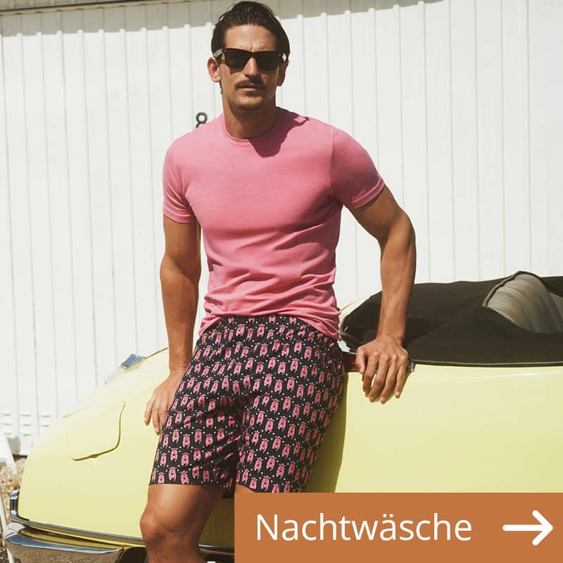 Ein Mann steht in einem kurzen Schlafanzug an ein Auto gelehnt.